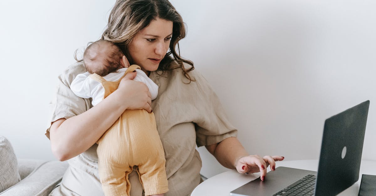 Can you rearrange items without using touch? - Concentrated young female freelancer embracing newborn while sitting at table and working remotely on laptop at home