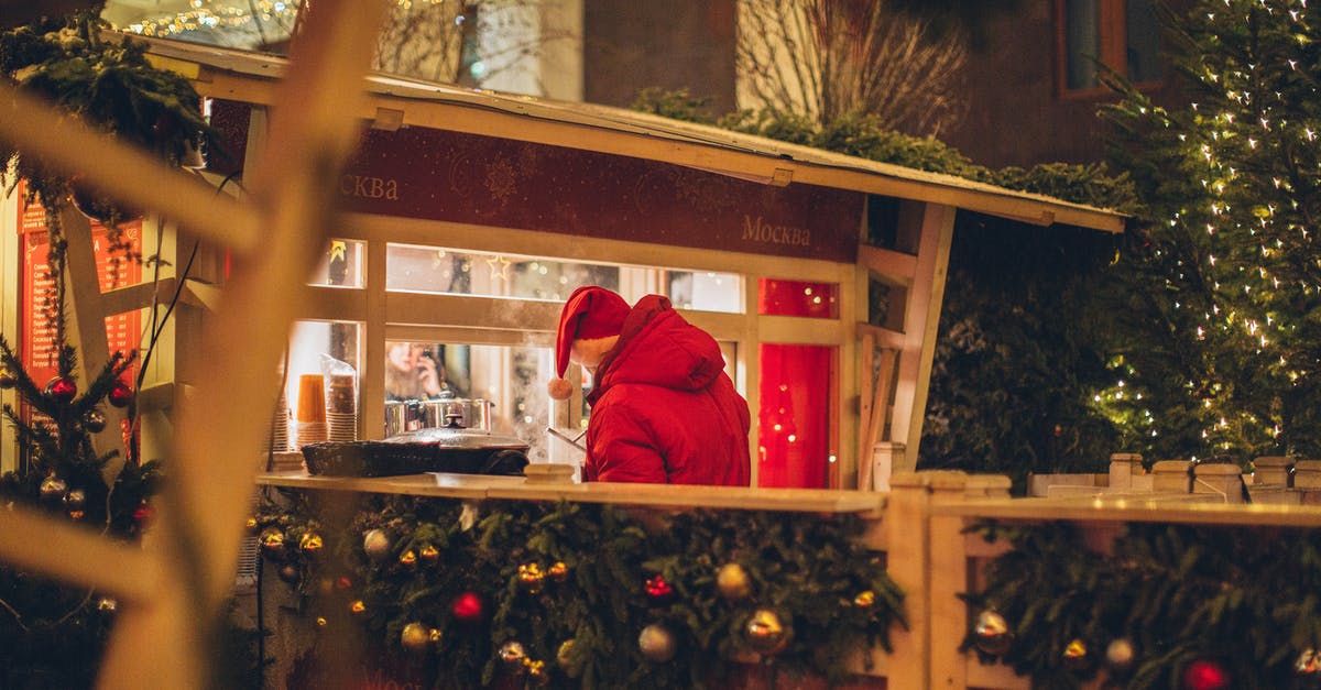 Cannot buy stockpile items anymore – even if they are available! - Back view of male wearing warm outerwear standing near counter at Christmas fair while enjoying holidays and purchasing takeaway beverage in illuminated city
