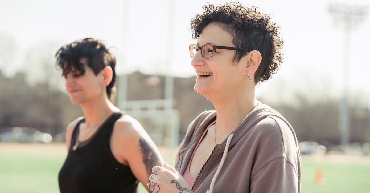 Chances of Hidden Ability through breeding, as well as chances for gender - Side view of couple of girlfriends in activewear jogging while cheerful female athlete laughing with androgynous female at stadium in back lit in daytime
