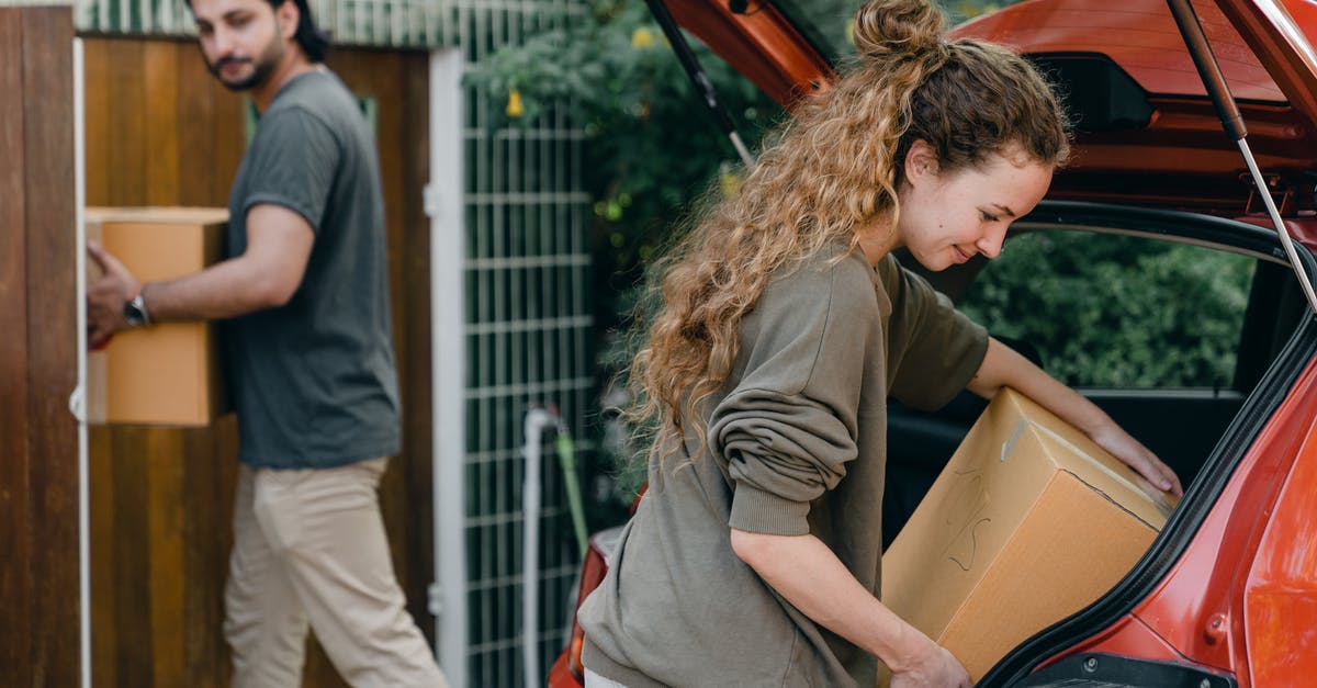 Change Email and password + New Account - Multiethnic young couple in casual wear taking carton boxes out of automobile trunk near newly bought house on summer day