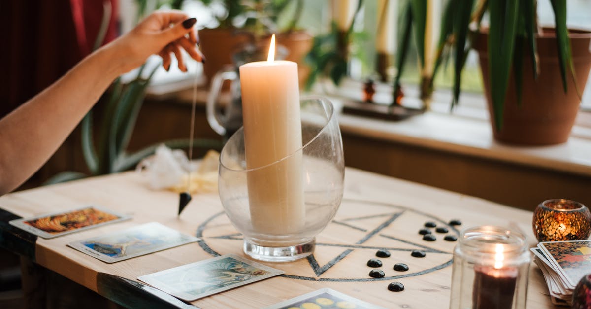 Changing the fate - Crop unrecognizable female fortune teller with amulet near tarot cards and shiny candles during prediction process at home Changing the fate - Crop unrecognizable female fortune teller with amulet near tarot cards and shiny candles during prediction process at home