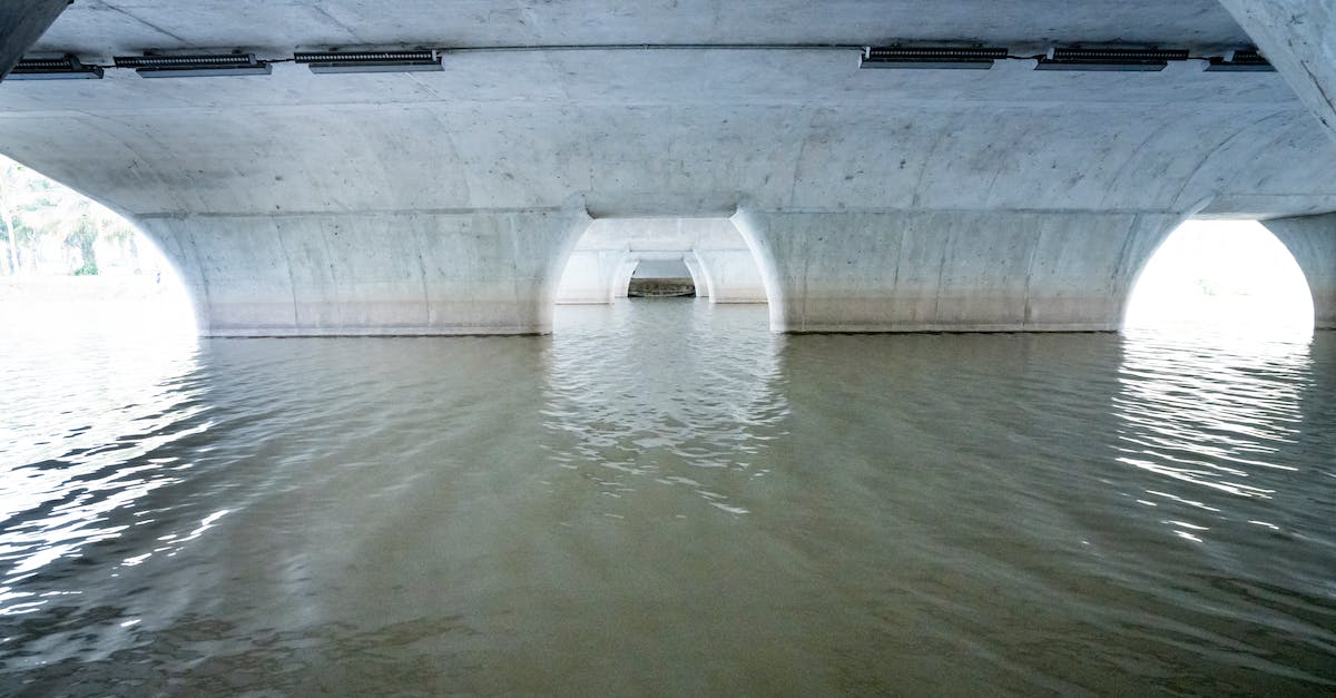 Channelling/digging under a bridge - Area under concrete white bridge with arched piers situated on rippling river on sunny day