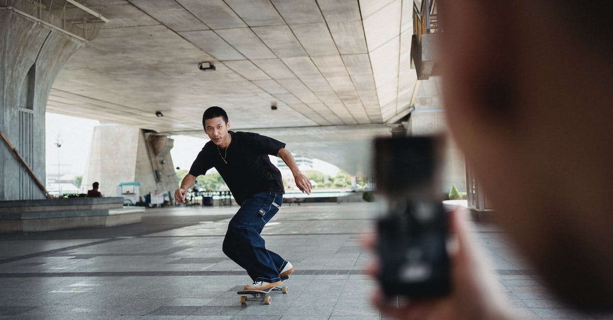 Chaos Frame penalty for taking no action in training - Full body of sportive man riding on skateboard under bridge and looking at camera of smartphone during training in street Chaos Frame penalty for taking no action in training - Full body of sportive man riding on skateboard under bridge and looking at camera of smartphone during training in street