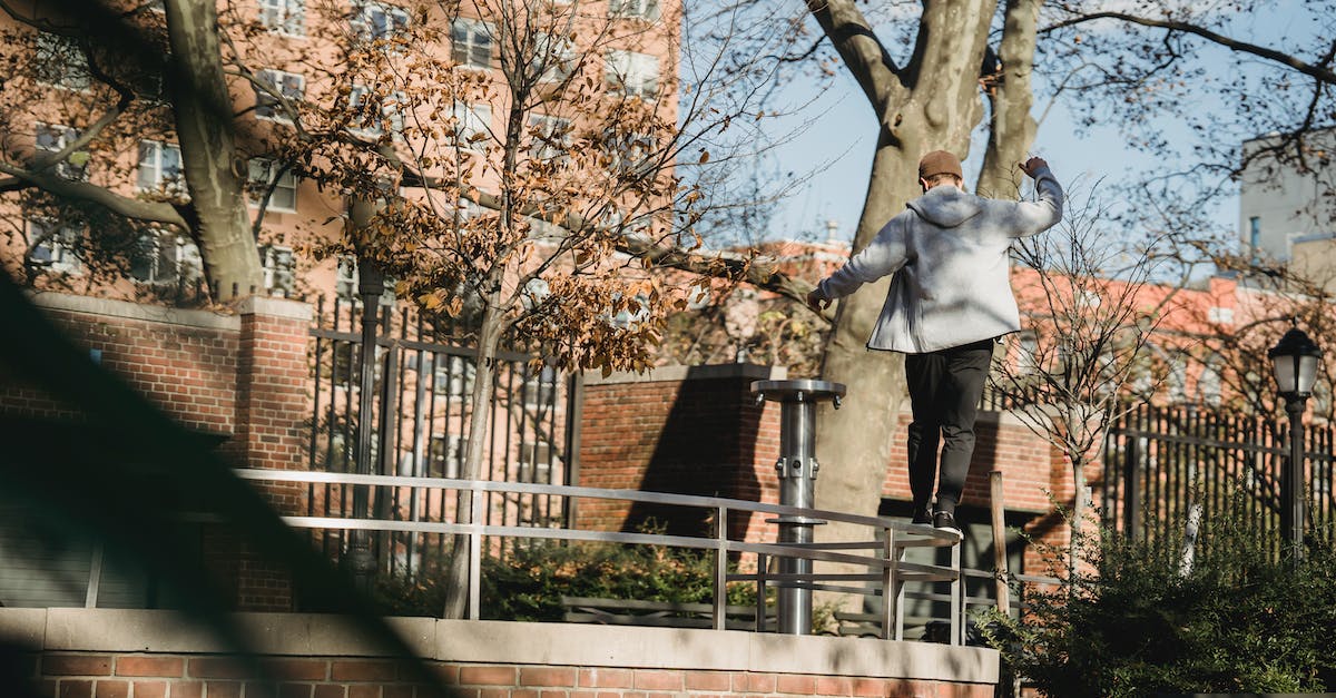 Cheapest/fastest way to raise a Mind Mag? - Back view of male in casual clothes walking on top of metal fence of brick construction on city street in residential district in sunny day