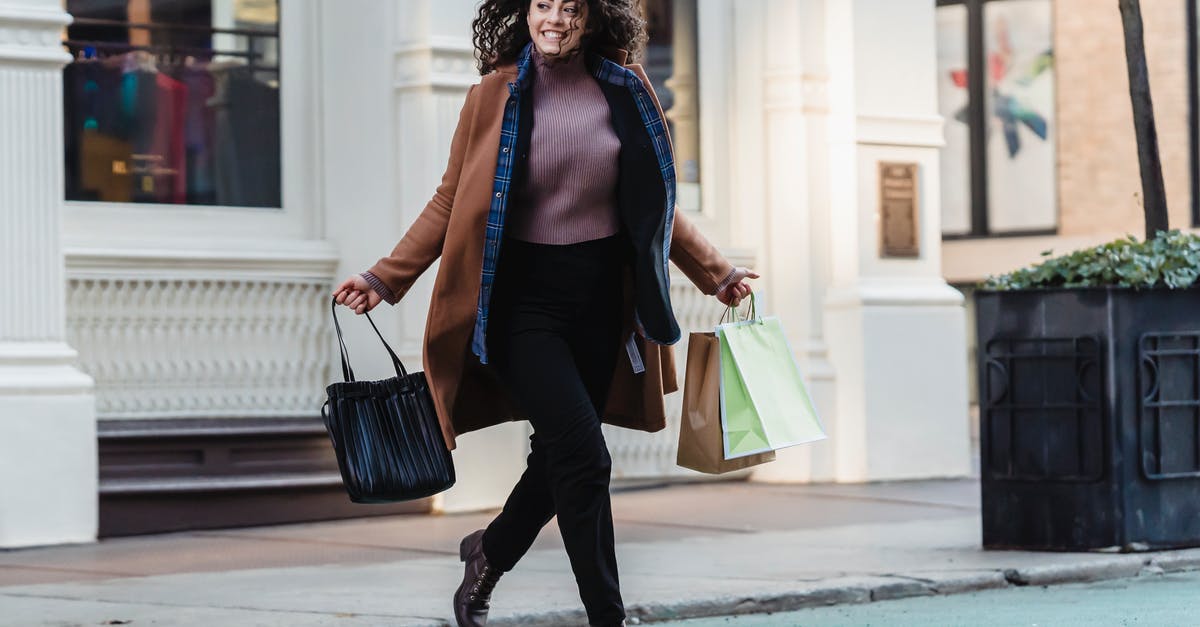 Cities Skylines - Not enough goods and not enough purchasers - Full body of smiling ethnic female in stylish outfit with shopper bags in hands running on road near building in city