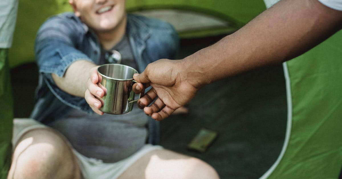 Clash of Clans: Take a break - Crop anonymous African American man taking camping metal cup from cheerful friend sitting in tent in daytime Clash of Clans: Take a break - Crop anonymous African American man taking camping metal cup from cheerful friend sitting in tent in daytime