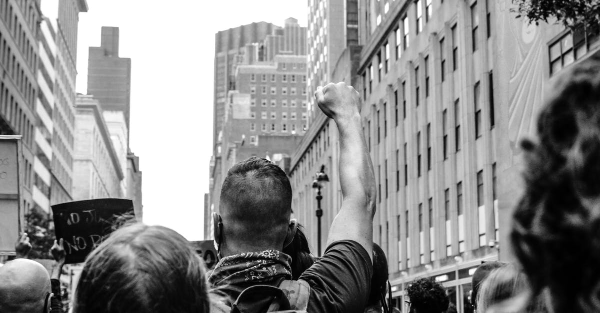 Cloak the power surge or the missiles in the Rebel Flagship fight? - Black and white back view of crop anonymous activists with fist up fighting for social rights between urban buildings