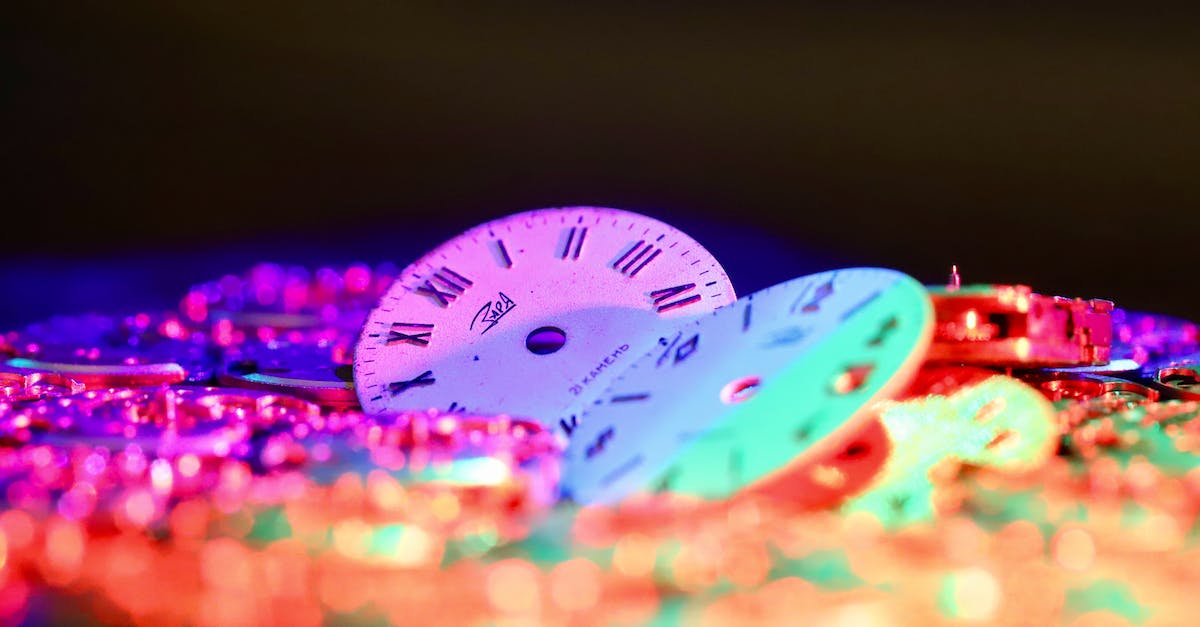 Clock with 2 different times - Round clock faces with Roman and Arabic numerals placed among stack of watch movements in dark room on black background Clock with 2 different times - Round clock faces with Roman and Arabic numerals placed among stack of watch movements in dark room on black background