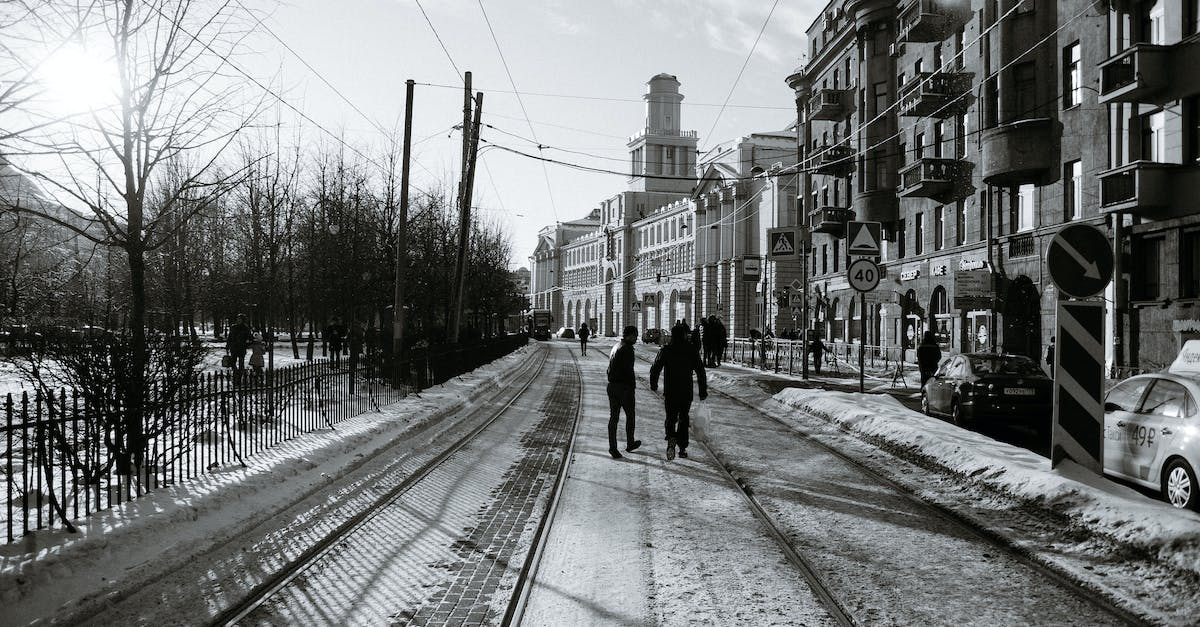 Clothing or stone houses for the winter? - Black and white back view of anonymous male strolling on tramway between old urban house facades and leafless trees in winter