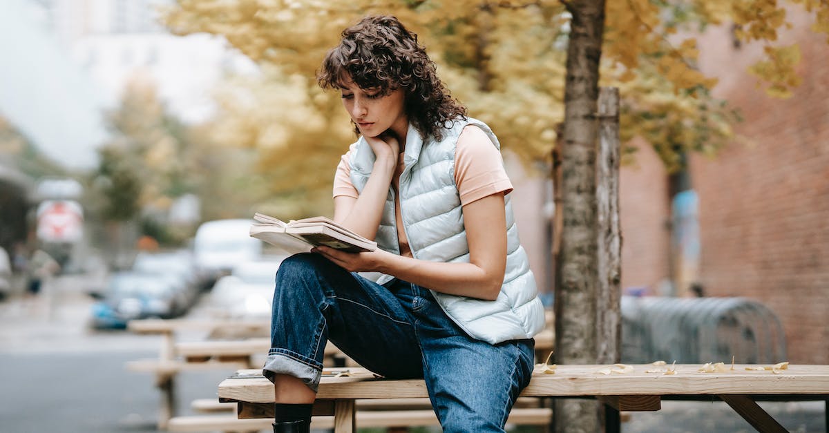 Constant crashes near Whiterun - Pensive female in trendy outfit reading book while sitting on wooden table near autumn tree on city street in daytime