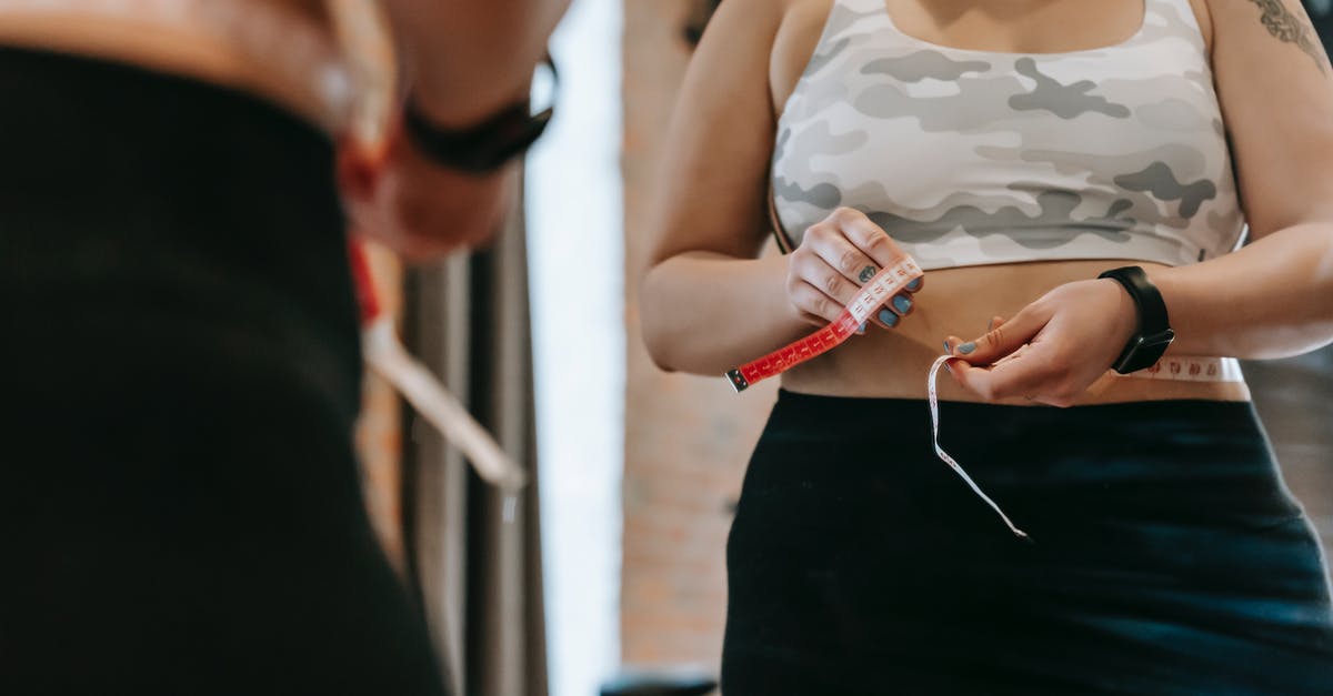 Control Landing on Stomach vs Back - Woman measuring waist with tape in gym Control Landing on Stomach vs Back - Woman measuring waist with tape in gym