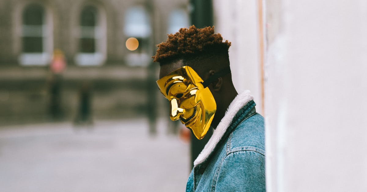 Corruption of GLaDOS - Side view of thoughtful African American activist wearing golden Anonymous mask as symbol of protest against current state policy standing near building on city street in daytime Corruption of GLaDOS - Side view of thoughtful African American activist wearing golden Anonymous mask as symbol of protest against current state policy standing near building on city street in daytime
