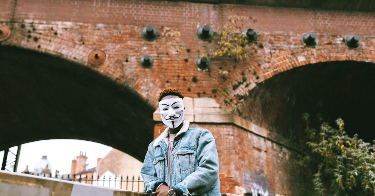 Corruption of GLaDOS - Black man in Anonymous mask standing against brick construction Corruption of GLaDOS - Black man in Anonymous mask standing against brick construction