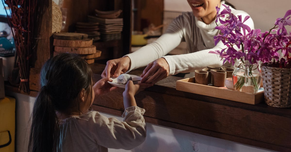 Counter Little Mac KO Punch - Crop Asian female bartender wearing apron standing behind wooden counter in cozy cafeteria while giving delicious dessert to little girl customer Counter Little Mac KO Punch - Crop Asian female bartender wearing apron standing behind wooden counter in cozy cafeteria while giving delicious dessert to little girl customer