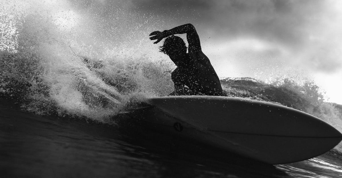 Crash to desktop when approaching Atlantis Latomia - Black and white of anonymous male surfer riding on wave with raised arm against cloudy sky in stormy weather outside