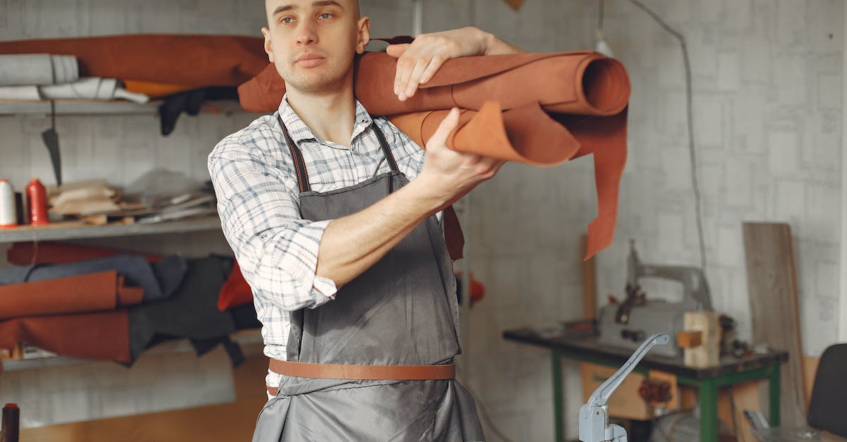 Create Official Dedicated CS:GO Server - Serious focused craftsman in apron and gray check shirt standing with brown leather roll on shoulder while working in professional workshop and looking away pensively