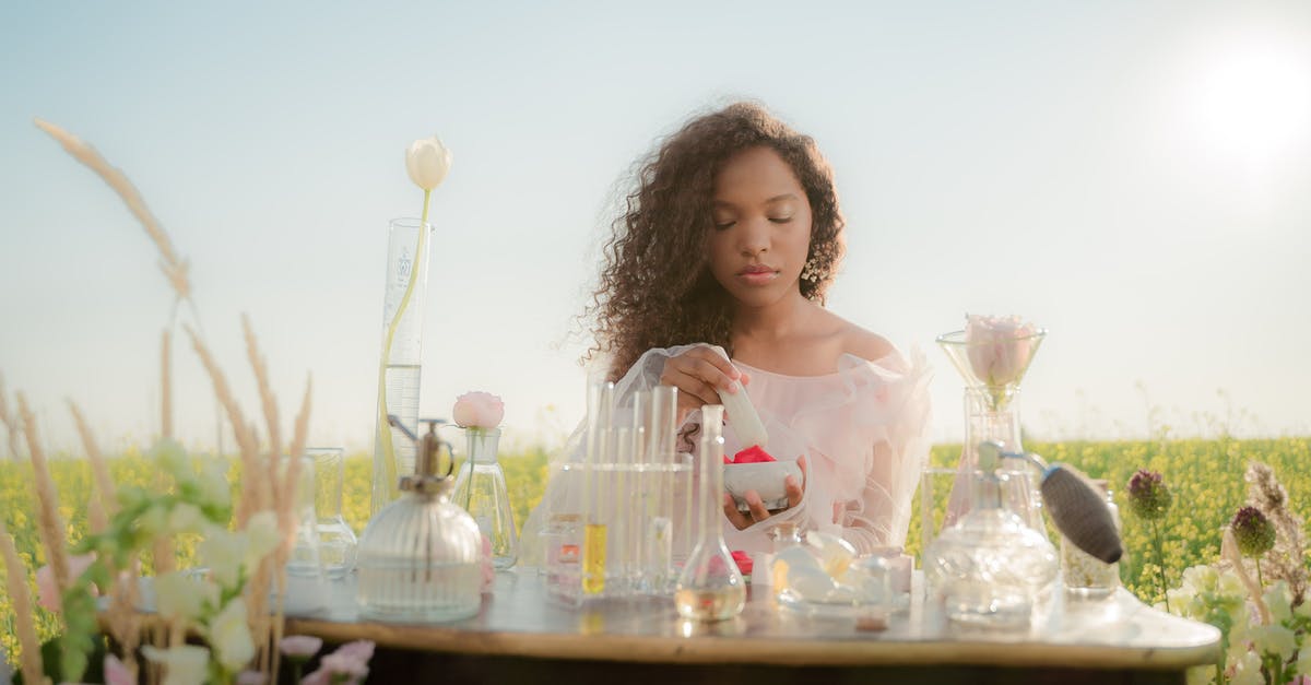 Creating space vacuum - Woman Sitting at Table in Middle of Meadow and Producing Perfumes from Flowers
