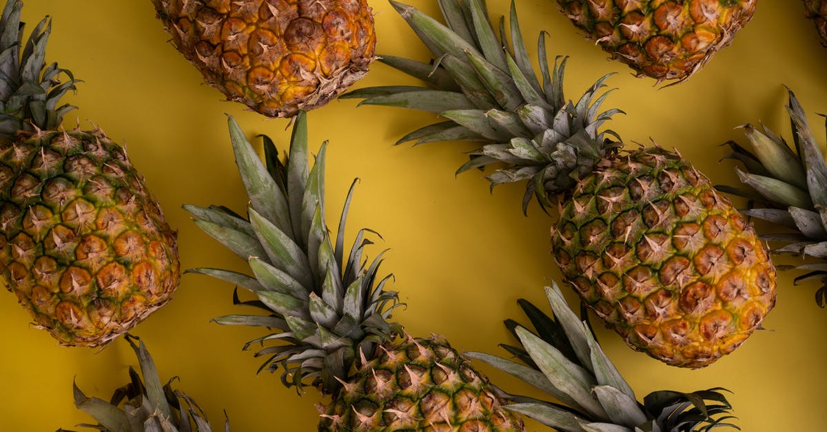 Crown summoned too many octopi - Top view of whole fresh pineapples with green leaves and brown skin arranged on yellow background in modern light studio
