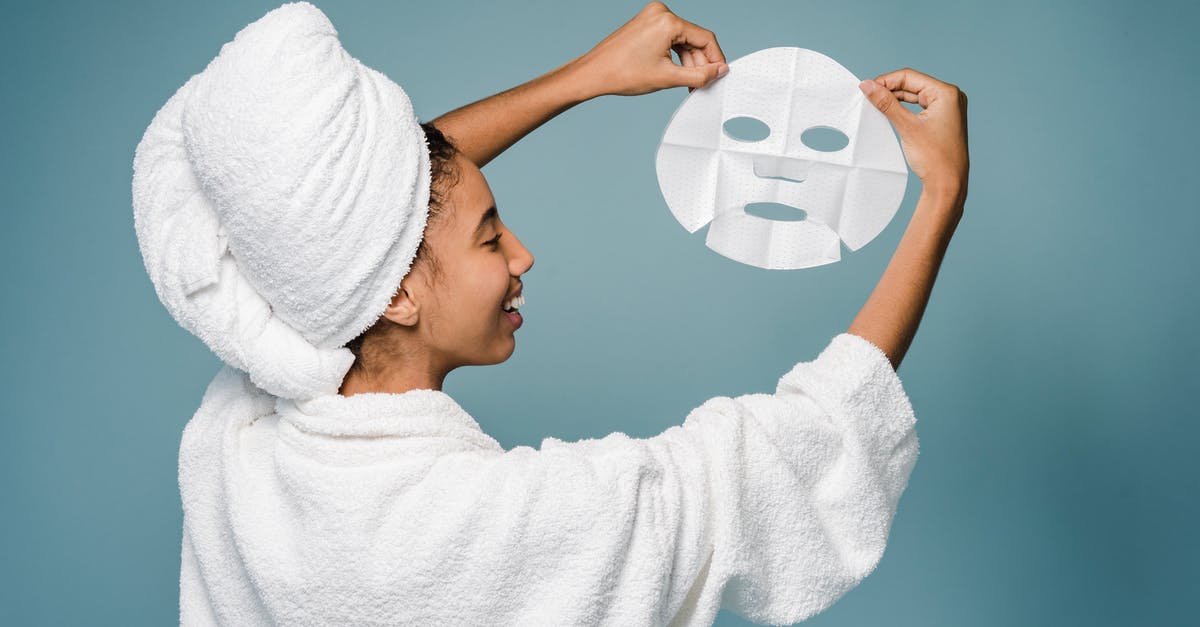Daily challenge not showing - Back view of happy young African American female in bathrobe with towel on head smiling while demonstrating skin care mask against blue background Daily challenge not showing - Back view of happy young African American female in bathrobe with towel on head smiling while demonstrating skin care mask against blue background