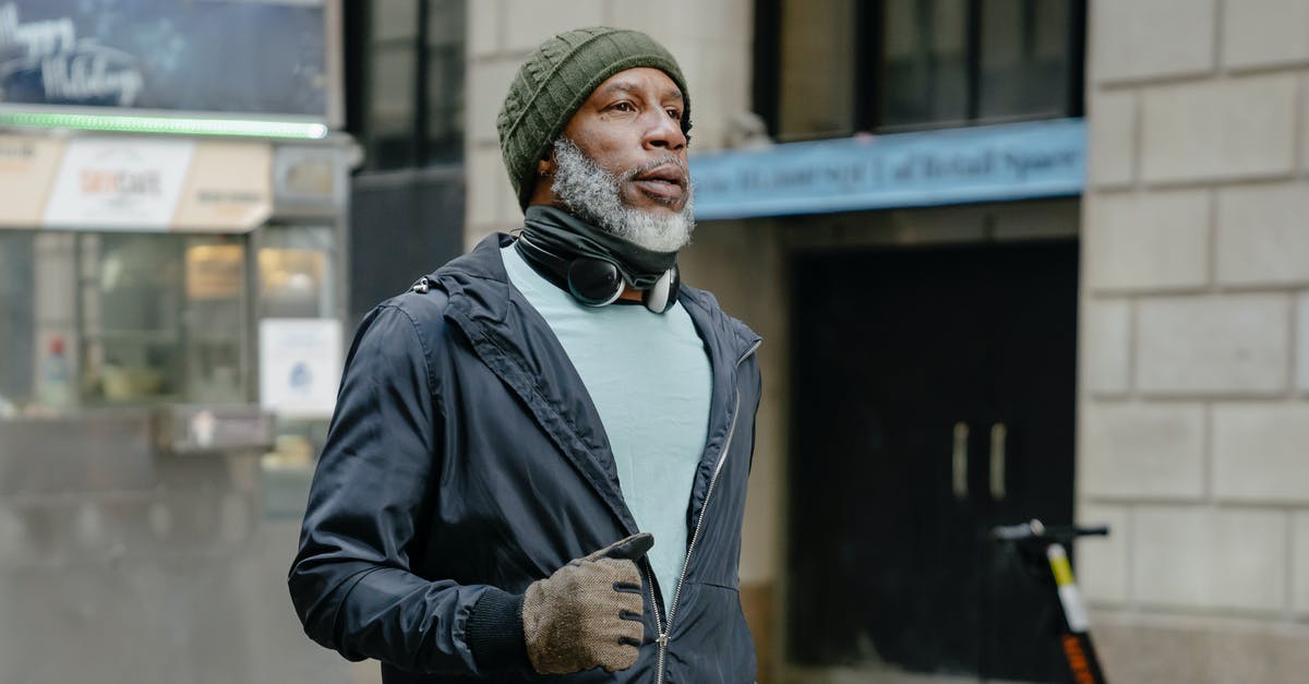 Daredevil Run not appearing - Serious African American bearded male in knitted hat and windbreaker jacket and headphones on neck running in street