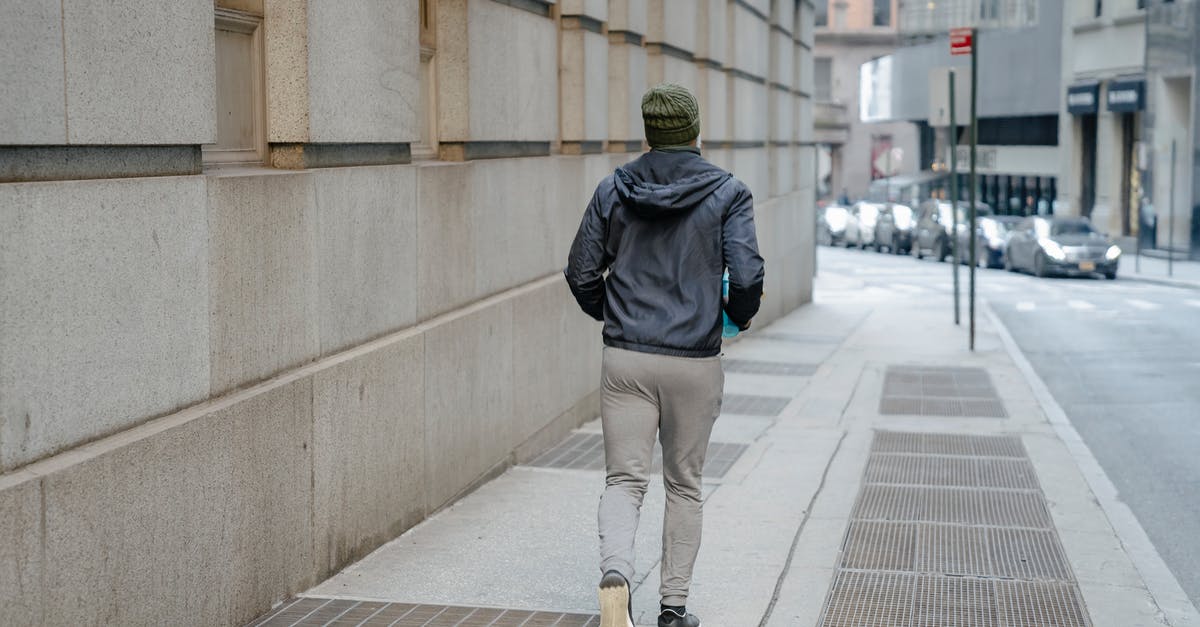 Daredevil Run not appearing - Back view of full body anonymous male wearing windbreaker jacket and gray sweatpants and knitted hat runnning on paved walkway along building Daredevil Run not appearing - Back view of full body anonymous male wearing windbreaker jacket and gray sweatpants and knitted hat runnning on paved walkway along building