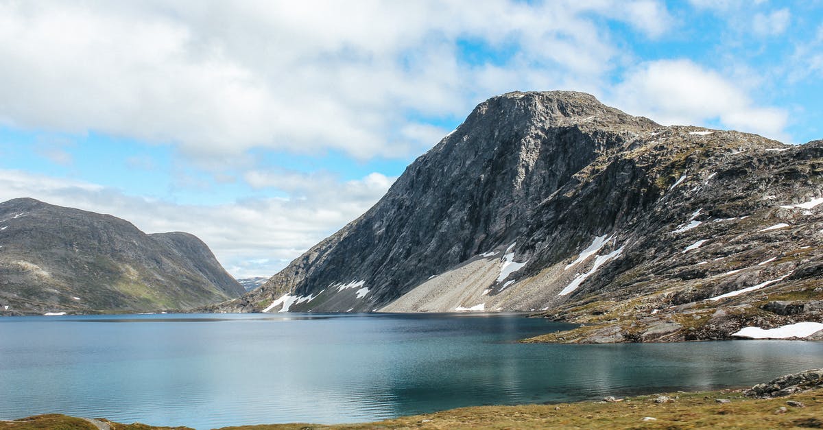 Defeated elite four, but somehow missed Blue’s mega stones. Can they still be gotten? - Grassy shore near calm lake surrounded by rough rocky cliffs against blue sky with clouds in coastal area in nature
