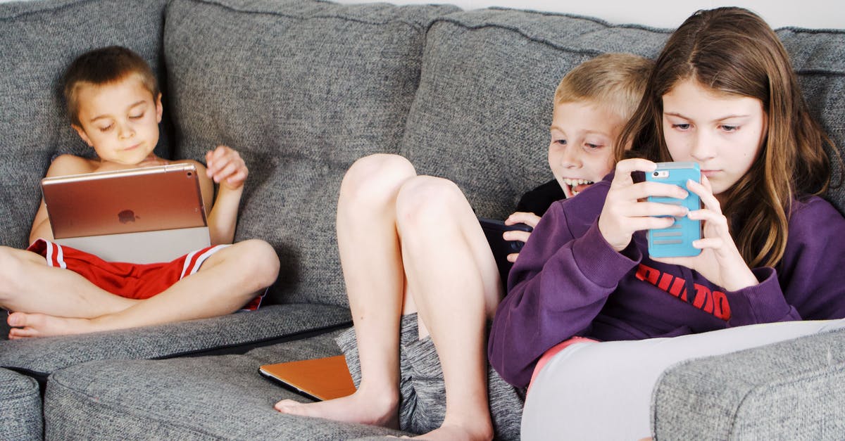 Definition of Mobile Games - Positive barefoot children in casual wear resting together on cozy couch and browsing tablets and smartphones