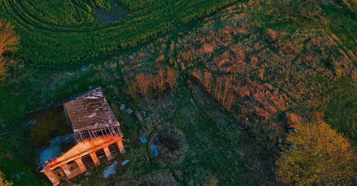 Destroy all farms or not? - Aerial view of abandoned house with destroyed roof located on green grassy field in countryside during sunset Destroy all farms or not? - Aerial view of abandoned house with destroyed roof located on green grassy field in countryside during sunset