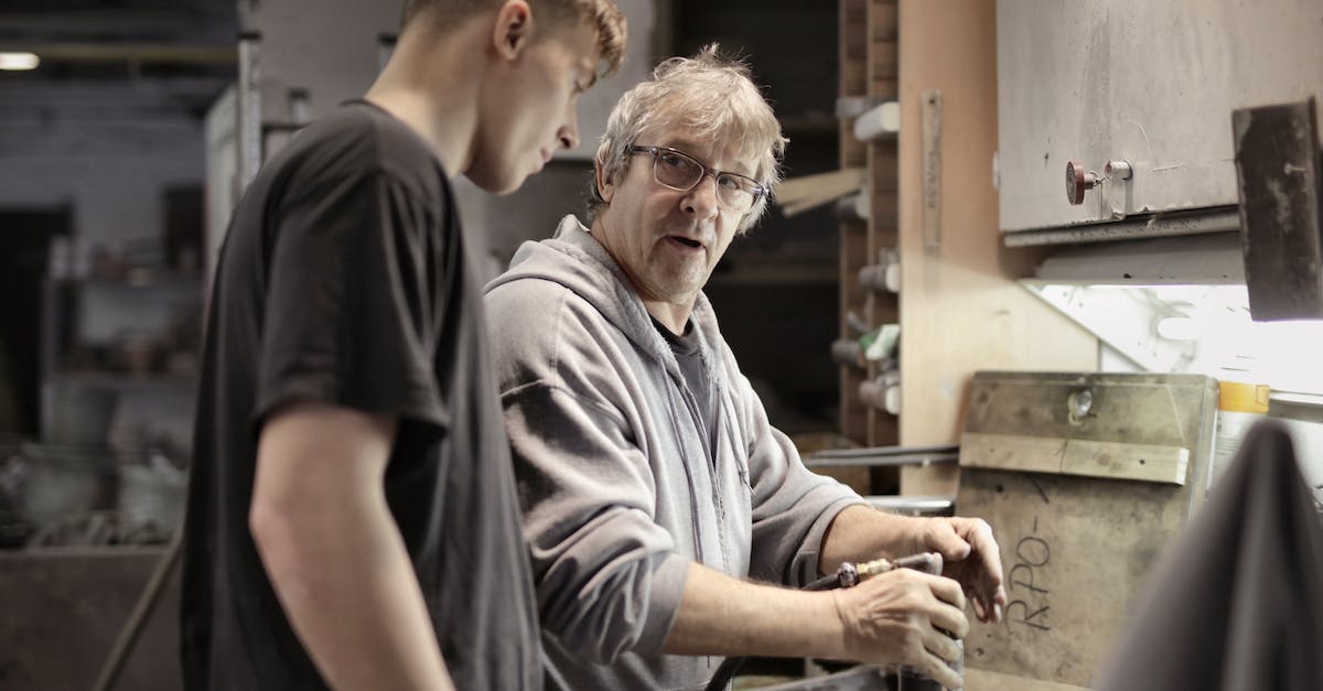 Diablo 3 Apprentice Mode/System? - Side view of senior foreman in eyeglasses showing to trainee how handling detail in workshop Diablo 3 Apprentice Mode/System? - Side view of senior foreman in eyeglasses showing to trainee how handling detail in workshop