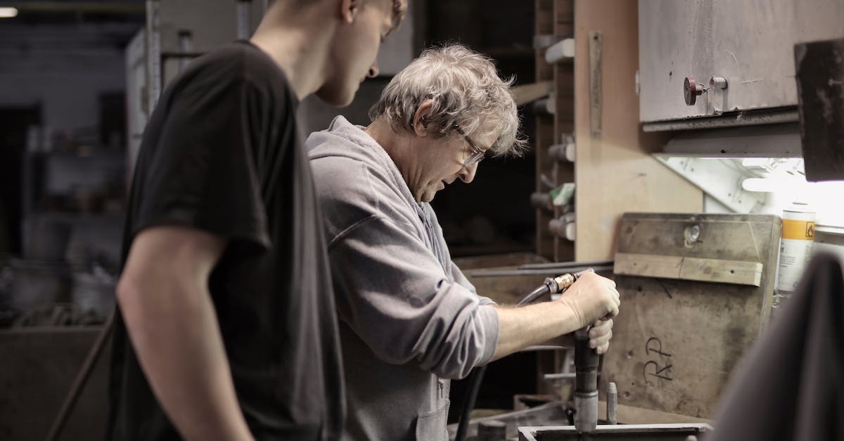 Diablo 3 Apprentice Mode/System? - Side view of senior artisan in eyeglasses handling detail in workshop while apprentice looking at process Diablo 3 Apprentice Mode/System? - Side view of senior artisan in eyeglasses handling detail in workshop while apprentice looking at process