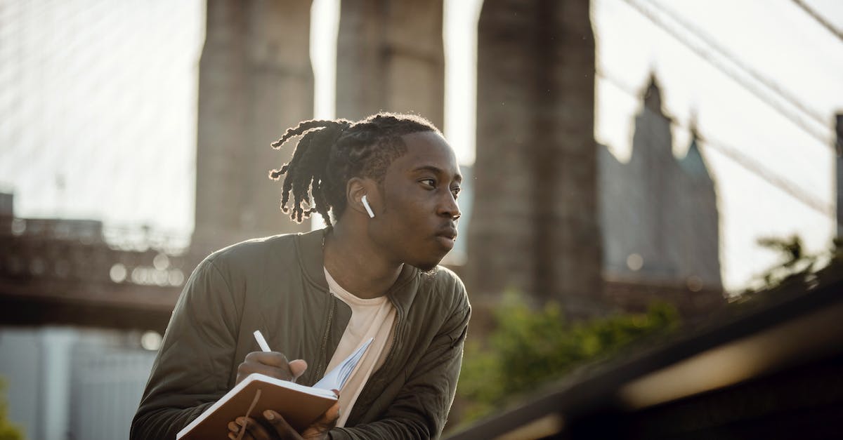 Disconnect Bridge From Lever - Positive black man listening to music with wireless earphones and taking notes in diary on street