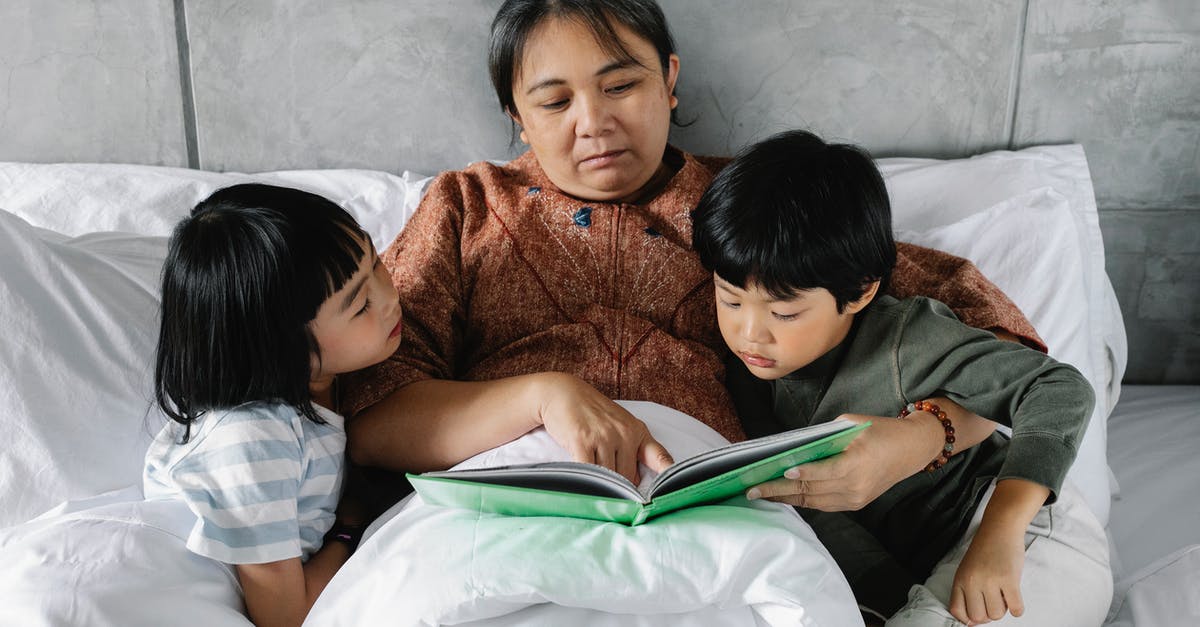 Do compasses still point towards your spawn/bed? - From above of focused elderly Asian woman lying in comfortable bed and reading interesting book for attentive little grandchildren