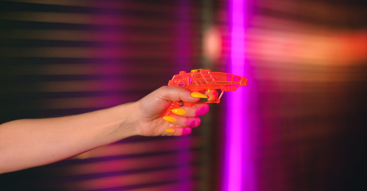 Do Defense Drones shoot down Flak projectiles? - Crop anonymous female with manicured hand pointing toy gun against neon lights in dark studio