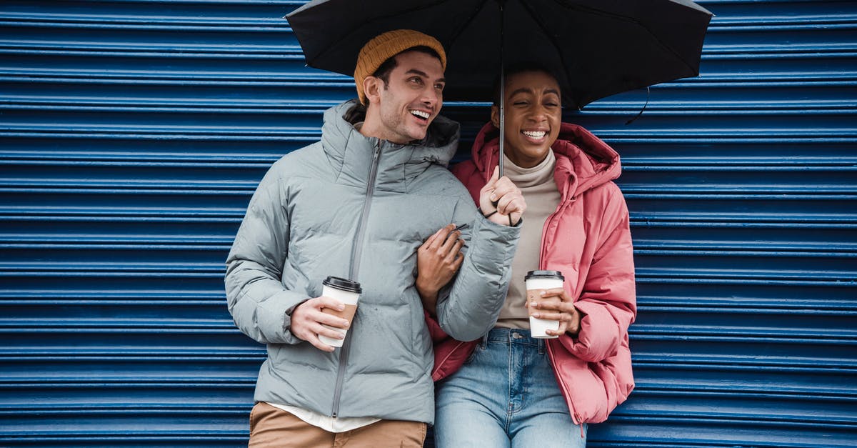 Do expeditions have an expiration date? - Happy multiracial couple with umbrella in warm outerwear laughing while standing on street with takeaway beverages in cold rainy weather