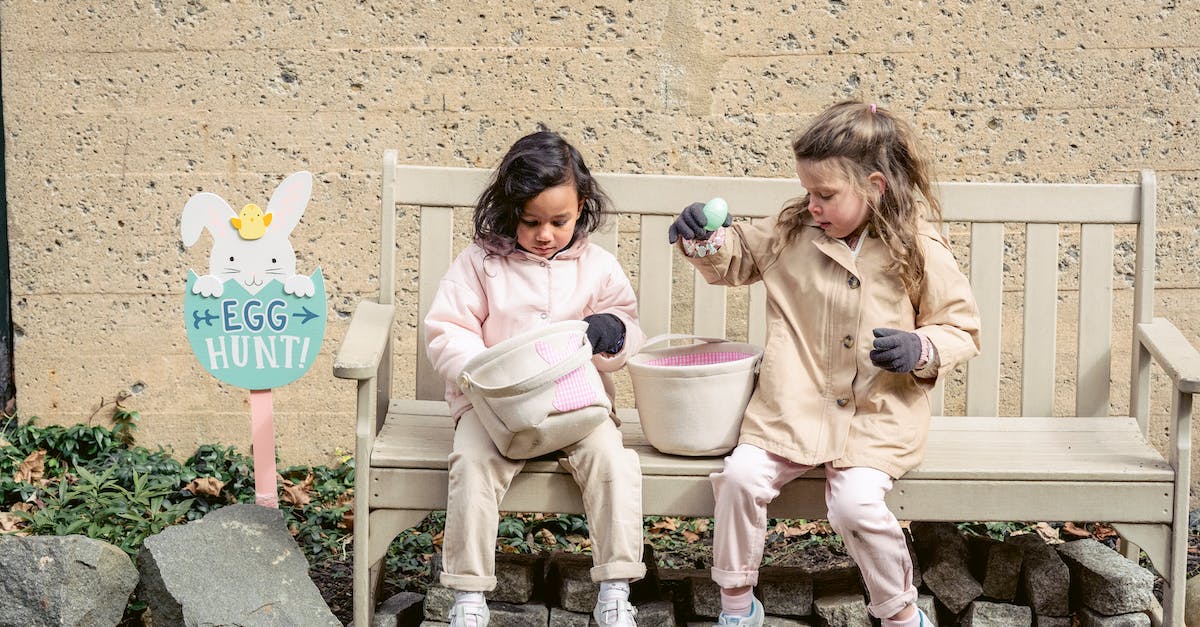 Do goblins activate spring traps? - Full body positive cute diverse girls in warm clothes playing with Easter eggs and sitting on bench in backyard