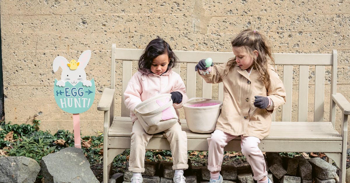 Do I have to reorganize plans every season? - Full body positive cute diverse girls in warm clothes playing with Easter eggs and sitting on bench in backyard