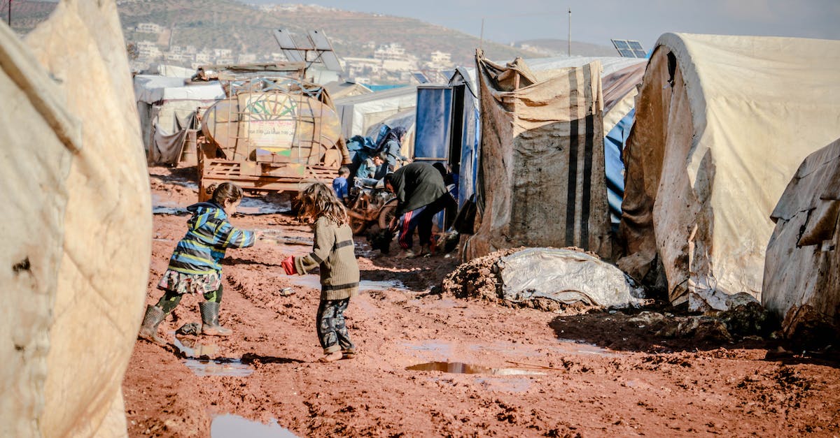 Do I need to play the first game? - Side view of little children playing in mud surrounded with shabby tents of poor settlement