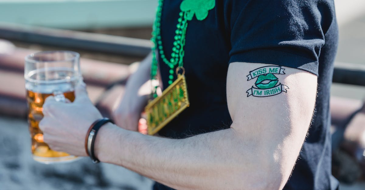 Do Luck-J and Mug synergise? - Side view of crop anonymous male with creative Kiss Me Im Irish tattoo on arm in casual clothes and shamrock necklace drinking mug of cold beer during St Patricks Festival