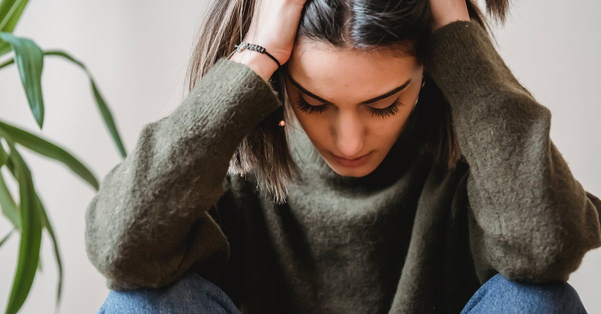 Do other endgame crisis appear if I am already the crisis? - Crop disappointed young ethnic female with dark hair in casual clothes grabbing head with hands and looking down while sitting against white wall at home