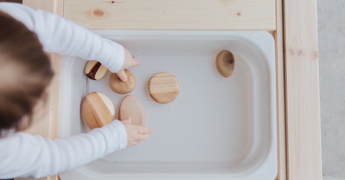 Do PS Vita backups contain activation info? - From above view of unrecognizable little child playing with wooden round stones in white plastic container at wooden table at home
