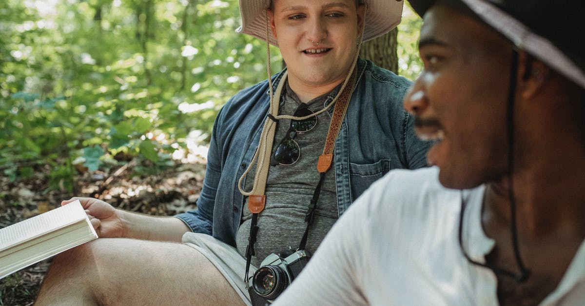 Do relationships degrade over time? - Smiling bearded African American man in black hat looking over shoulder on man while sitting together on blurred background in woods