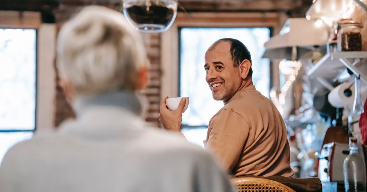 Do relationships degrade over time? - Back view of unrecognizable female in casual clothes speaking with happy middle aged ethnic husband drinking coffee at home
