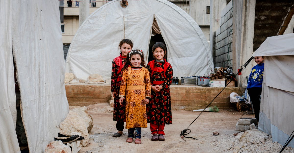Do settlers need ammunition? - Three Girls in Floral Dresses Smiling and Standing Near White Tent