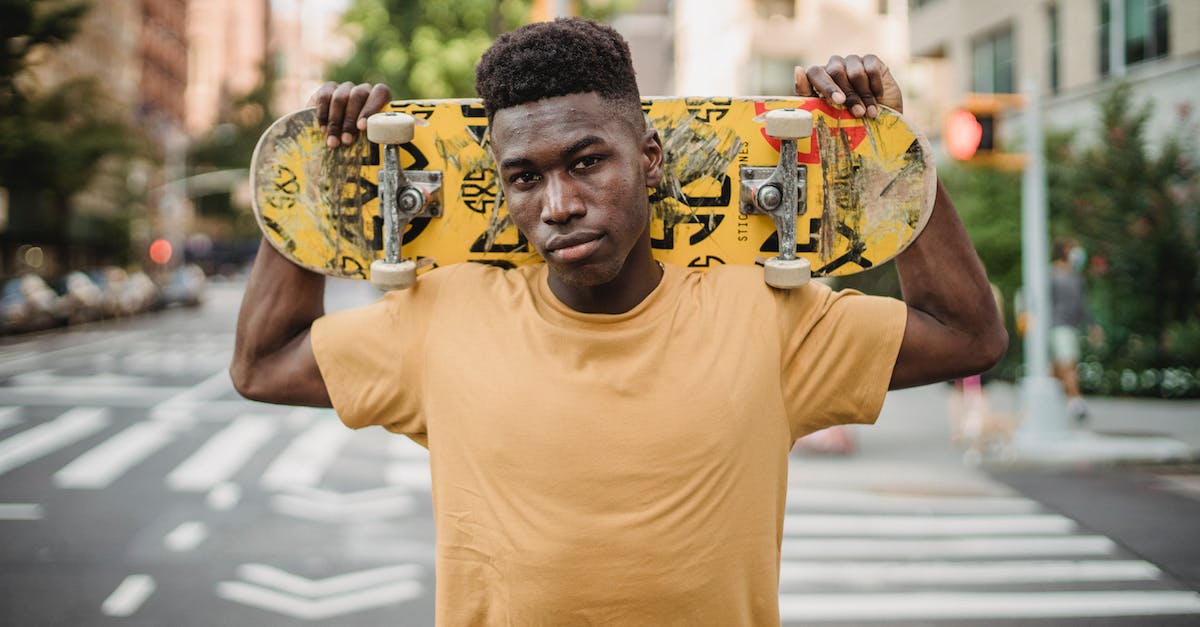 Do skills carry over with levels? - Serious young African American male skater with skateboard on shoulders standing on pavement near road and looking at camera