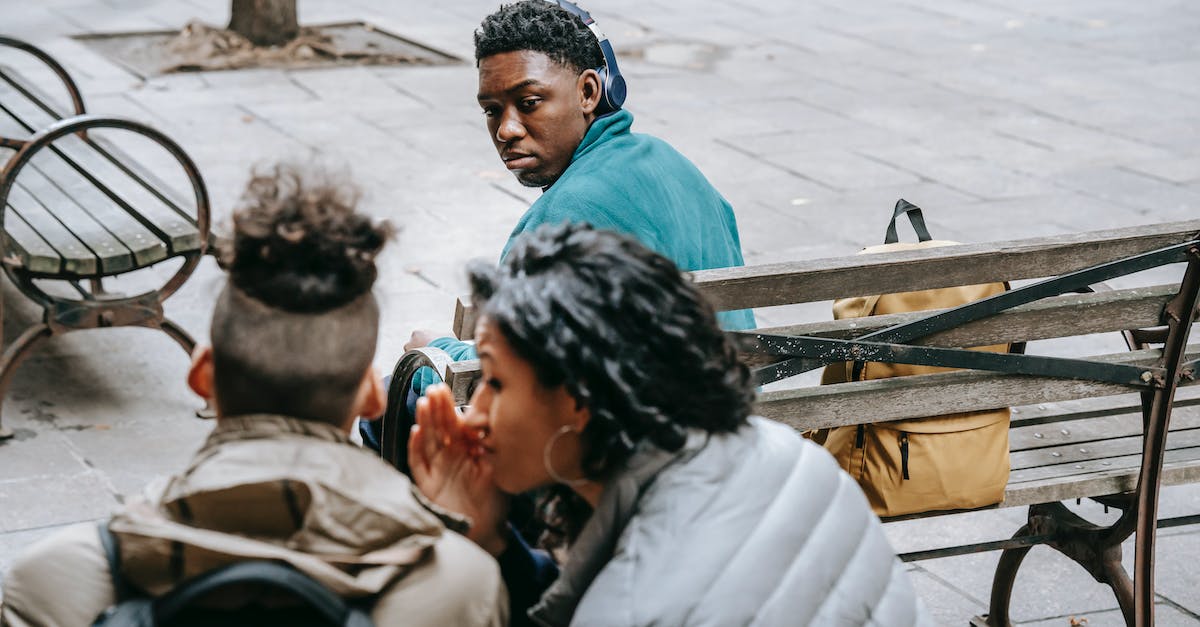 Do Titans have a weak point? - Back view of faceless classmates spreading gossip about African American man on wooden bench Do Titans have a weak point? - Back view of faceless classmates spreading gossip about African American man on wooden bench