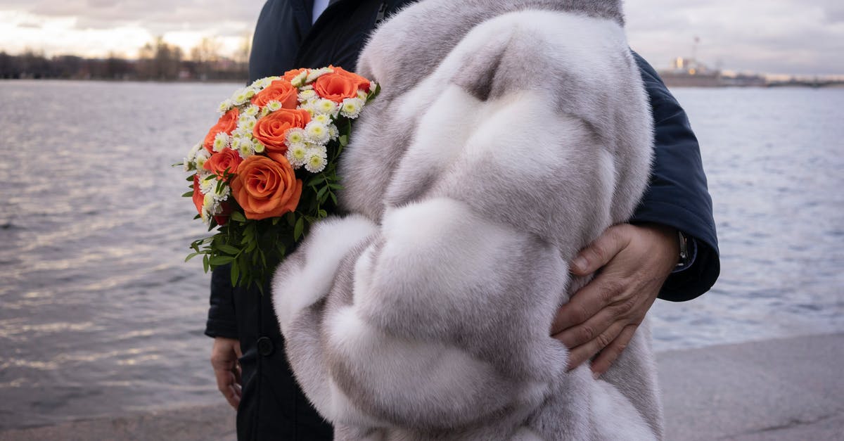 Do you have to water winter crops? - Unrecognizable male in suit hugging anonymous woman with flowers while standing on embankment near rippling water against cloudy sky in city