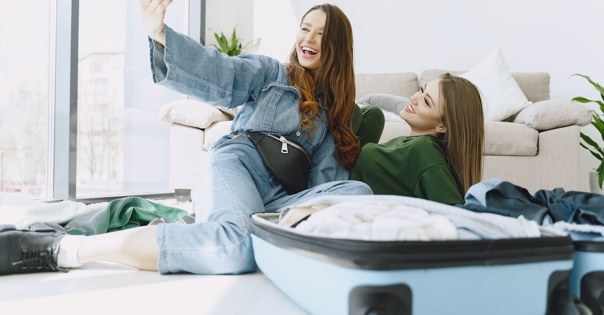 Do you need to be both level 20 and have the expansion pack 2 to unlock The Reef social place? - Happy young female friends in trendy outfits having fun and taking selfie while packing suitcase in cozy room