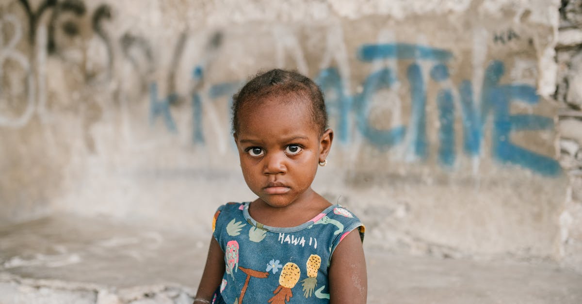 Do you need to build mining stations in your own territory? - Frowning African American girl near weathered concrete building with vandal graffiti and broken wall in poor district