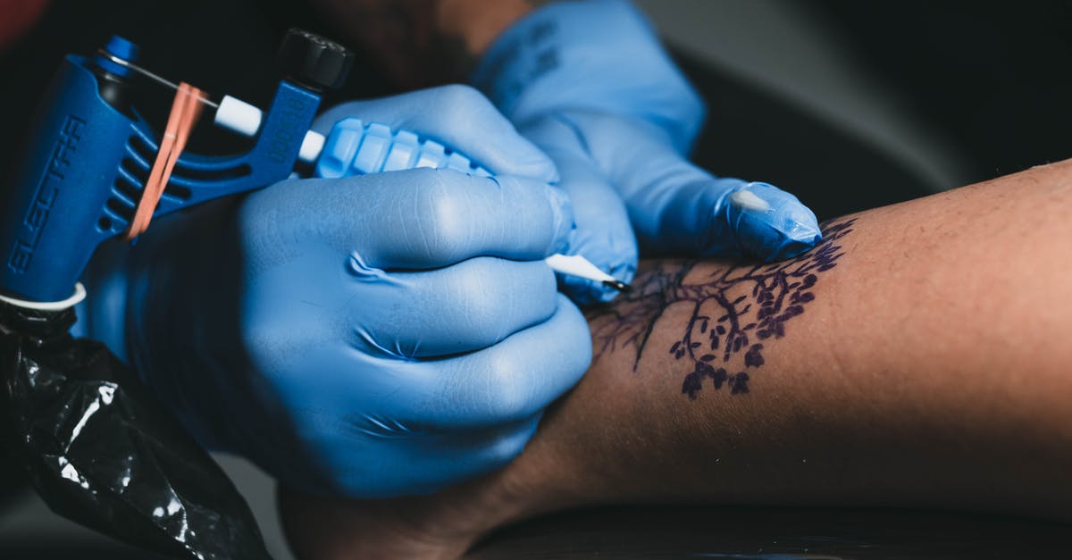 Does a dweller running around the room with his gun contribute to the attack? - From above of faceless tattooist in blue gloves applying tree tattoo with ink and professional machine on leg of anonymous client in salon