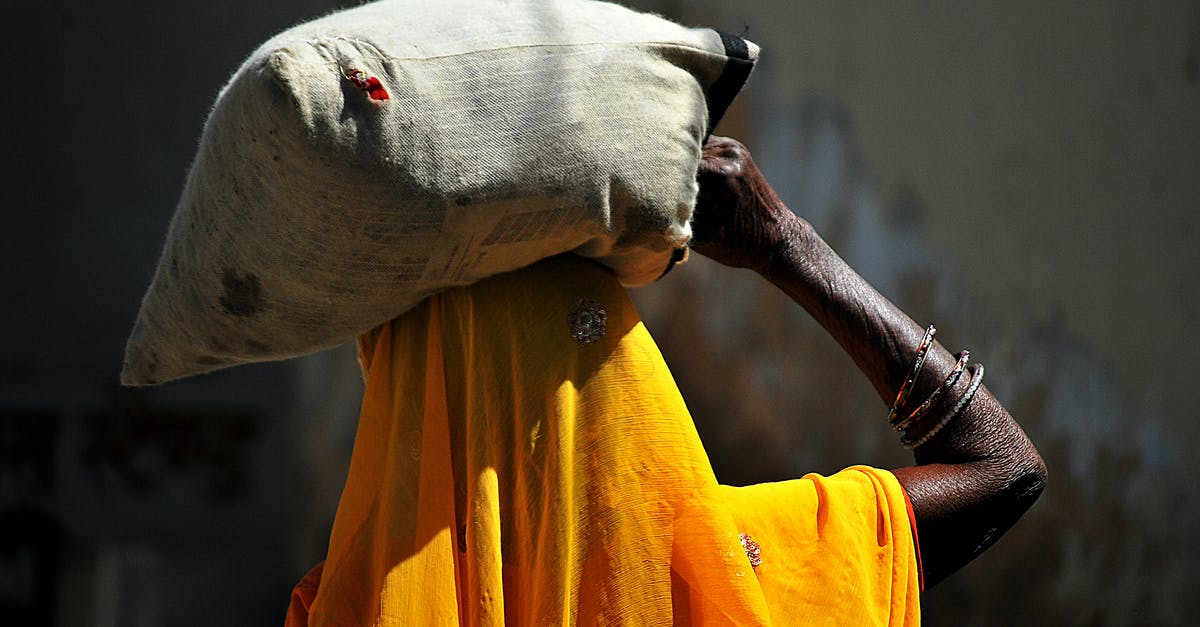 Does carry weight affect stealth? - Back view of unrecognizable African female in traditional yellow headscarf carrying heavy sack on head while walking in village on sunny day